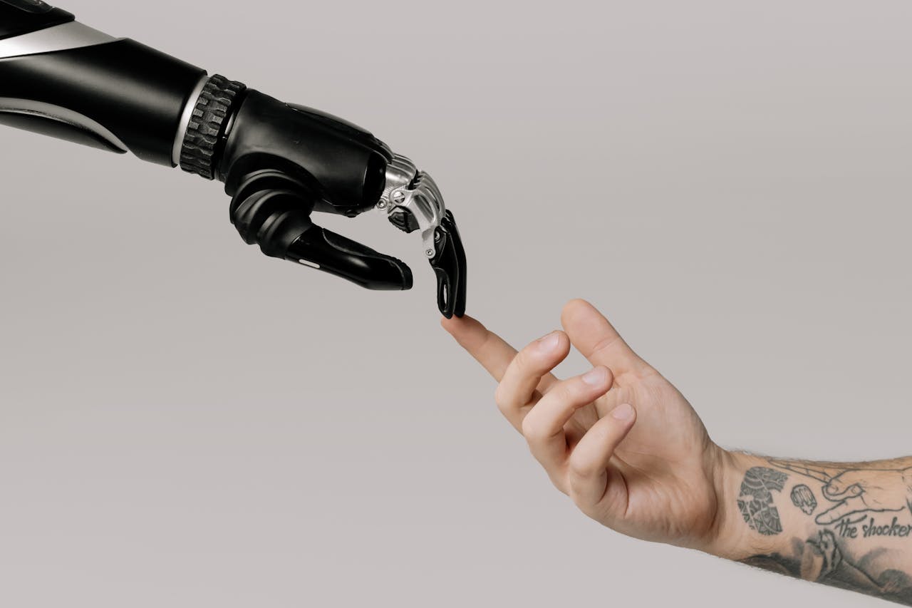 heros-img A human hand with tattoos reaching out to a robotic hand on a white background.
